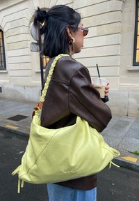 Sac à épaule en cuir vert citron avec une bandoulière tressée jaune, présentant un design décontracté et un logo doré à l'avant.