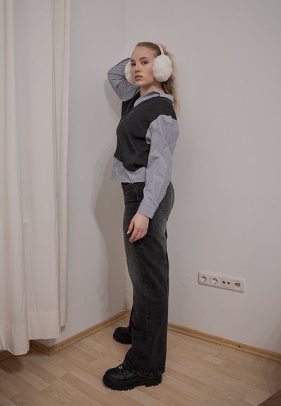 Top sin mangas de punto gris sobre una camisa de rayas azul y blanca, combinado con jeans acampanados negros y botas de plataforma negras; auriculares de peluche blancos.