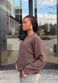 Rudas tekstūruotas megztinis laisvo kirpimo su ribinėmis rankogaliais. Derinamas su šviesiai pilkais džinsais, kuriuos puošia masyvi smėlio-rudos spalvos diržo detalė.