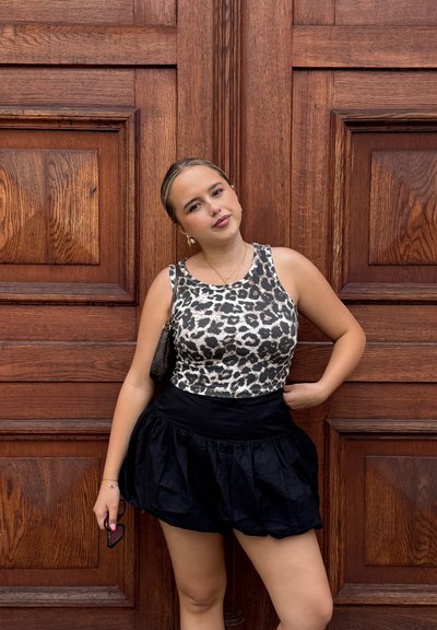 Top sin mangas de estampado de leopardo con un diseño ajustado, combinado con una mini falda negra y voluminosa. El fondo de paneles de madera añade textura.