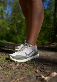 Běžecké boty Nike na trail, s světlě šedou síťovinou, zelenými akcenty, texturovanou podrážkou a reflexními prvky. Lankové šněrování a oranžová visačka v sadě.
