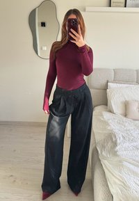 Bordeaux langærmet bluse med tætsiddende design, sammen med sorte brede bukser med snoreliv og spidse røde hæle.