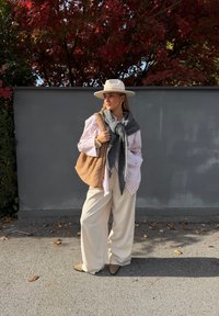 Hvit og rosa stripete skjorte, grått skjerf, beige bukser med vide ben og lysebrune ankelstøvler. Vevet brun veske. Bakgrunnen har rødt løvverk.