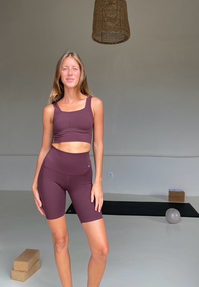 Conjunto atlético burdeos que incluye una camiseta corta con tirantes anchos y pantalones cortos de cintura alta. Tejido suave y elástico; diseño minimalista.