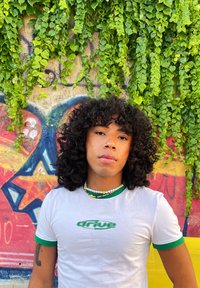 Λευκό T-shirt με πράσινες λεπτομέρειες, που φέρει το κείμενο "drive" σε πράσινη γραμματοσειρά. Πολύχρωμο κολιέ από χάντρες. Φόντο από πράσινα στοιχεία και γκράφιτι.