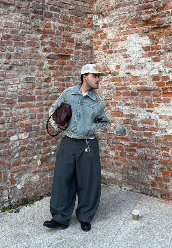 Denim jakna svijetloplave boje s prugama; labave sive hlače; smešna torba; crne cipele; pozadina od crvene opeke.