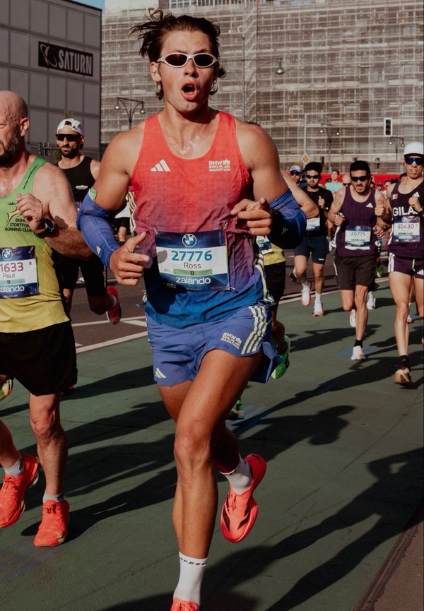 Corredor masculino con ropa roja y azul y dorsal 27776 corriendo en un maratón concurrido con otros corredores en una calle de la ciudad.
