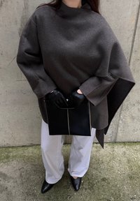 Brun ullponcho med vide ermer, kombinert med hvite bukser og svarte lærhansker. Svart rektangulær clutch med sølvdetaljer.