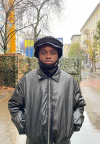 Svart vattentät jacka med dragkedja, bärs över en svart halskrage. En bredbrättad bucket hat används, med regndroppar synliga på ytor.