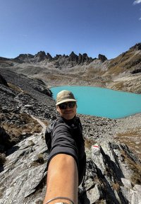 Mees päikeseprillides ja mütsiga teeb selfie kivisel mägirajal türkiissinise alpi järve lähedal selge sinise taeva all.