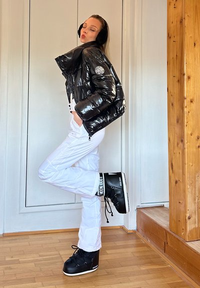 Chaqueta negra acolchada, pantalones de nieve blancos y botas negras de plataforma con cordones. Texturas suaves, contrastadas por materiales brillantes y acentos audaces.