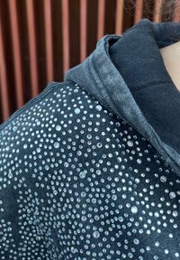Sweat à capuche en denim noir orné de strass transparents brillants disposés en motif dispersé sur un côté, tissu texturé avec un col côtelé.