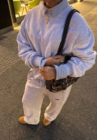 Γκρι υπερμεγέθη φούτερ και ταιριαστά παντελόνια φόρμας με κολάρο από μπλε καρό πουκάμισο. Μπεζ παντόφλες και μαύρη τσάντα ώμου με λεοπάρ σχέδιο.