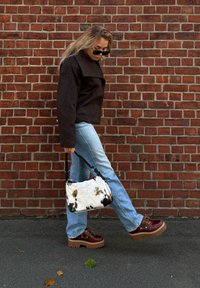 Τσάντα με σχέδιο από μαύρες και άσπρες κηλίδες της αγελάδας, με μαύρη ζώνη, φορεμένη με σκούρο μπουφάν και ανοιχτό μπλε τζιν, σε συνδυασμό με καφέ χοντρά παπούτσια.