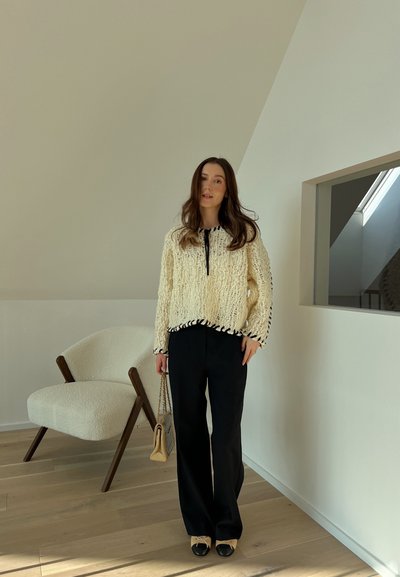 Suéter de mezcla de lana en color crema con ribetes negros, de corte holgado y con cuello ajustable. Combinado con pantalones de pierna ancha negros y zapatos en negro y beige.