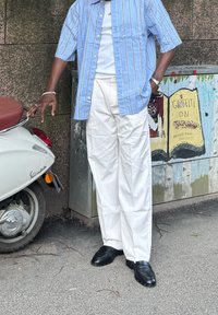 Vaaleansininen raidallinen nappipaita valkoisen t-paidan päällä, yhdistettynä valkoisiin housuihin ja mustiin kenkiin. Lähistöllä on vintage-tyylinen valkoinen skootteri.