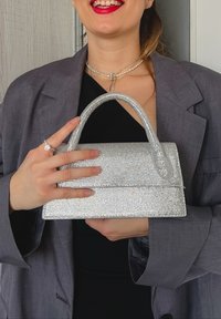 Ασημένια τσάντα με χάντρες με δομημένο σχέδιο, επίπεδη κορυφή και στρογγυλή λαβή. Λείο υφή με λαμπερά αξεσουάρ παντού.