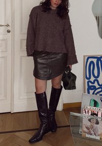 Μεγάλο μωβ πουλόβερ, μαύρη δερμάτινη μίνι φούστα, πράσινη τσάντα και γόβες μέχρι το γόνατο με γυαλιστερή υφή κροκοδείλου, τονισμένες από υφές.