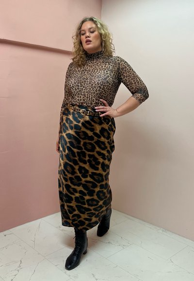 Top de leopardo transparente de manga larga combinado con una falda de satén de leopardo de longitud media. Botines negros y un cinturón a juego completan el look.