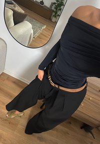 Sorte bukser med vide ben kombineret med en tætsiddende marineblå off-shoulder top. Inkluderer et brunt bælte og olivengrønne hæle. Glat tekstur og skræddersyet design.
