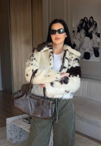 Vit och brun fuskpälsjacka med en kort design, svarta solglasögon och en brun läderhandväska, matchat med olivgröna byxor.