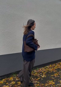 Bolsa de camurça castanha com uma forma estruturada e alças duplas, combinada com um suéter de malha azul-marinho e calças largas castanhas.