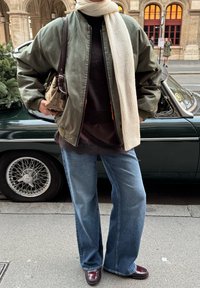 Grøn bomberjakke, sort top med blonderkant, lyseblå vide jeans, bordeaux sko og et cremefarvet tørklæde med en mønstret håndtaske.