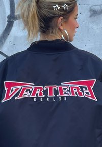 Μαύρο μπουφάν bomber με κόκκινο και λευκό ραμμένο λογότυπο "VERTER" και "BERLIN", διαθέτοντας λεία υφή και κλασικό σχέδιο.