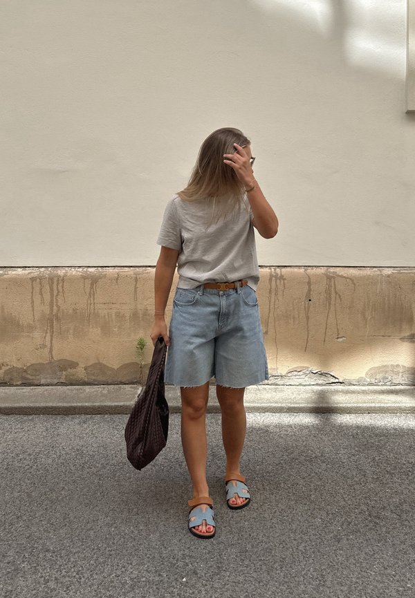 Gaiši pelēks T-krekls, zili denim atdzīvotāji, brūna josta un brūna austā soma. Iezīmētās ikdienišķās sandales ar ziliem siksniņām un oranžiem akcentiem.