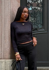 Zwart langhands T-shirt met een bootnek, gecombineerd met hoge zwarte broek. Accessoires zijn gelaagde gouden armbanden en een hangerslang.
