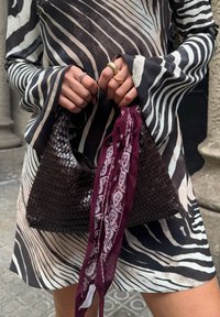 Tkana smeđa torba s zakrivljenim oblikom, uparen s bordo šalom sa bijelim paisley uzorcima. Model nosi haljinu s crno-bijelim prugama.