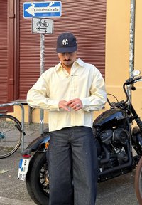 Világos sárga, gombos, finom csíkos mintával ellátott ing, hosszú ujjakkal és hímzett részletekkel. Sötétkék farmernadrág, ezüst ékszerek és egy NY sapka.