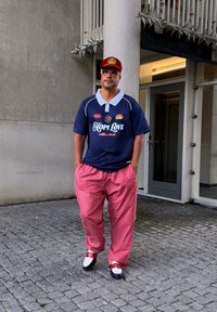 Polo navy con colletto bianco e testo "HOPI LOVE"; pantaloni larghi a scacchi rossi e bianchi; scarpe nero e bianche con dettagli rossi.