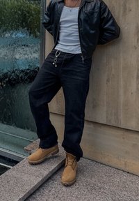 Černé džíny z denimu s volnějším střihem, bílý nátělník a přiléhavá černá kožená bunda. Hnědé kotníkové boty na tkaničky s texturovanou podrážkou.