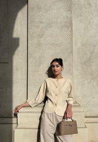 Beige linskjorte med knapper og avrundet nederkant, trekvartlange ermer, sammen med lyse beige linsbukser og en liten brun håndveske.