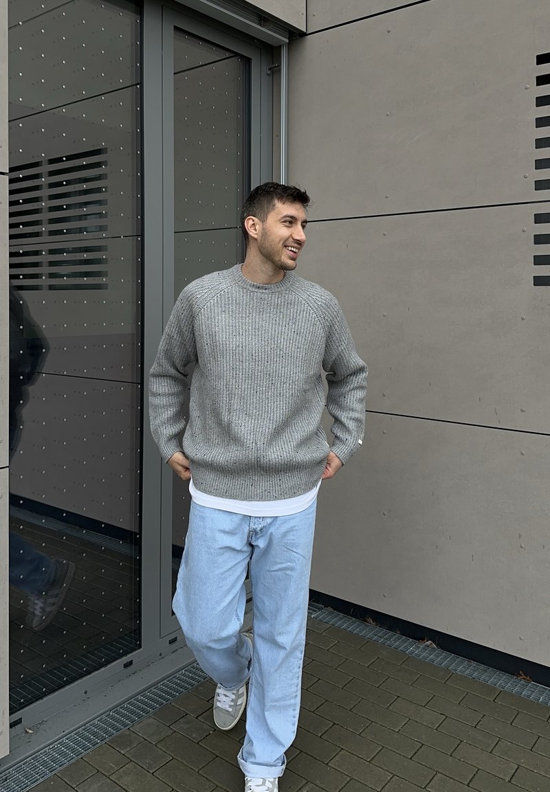 Pull en maille grise avec un motif texturé, accompagné d'un jean bleu clair. Le décor présente des matériaux et un design modernes.