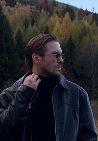 Zwarte leren jas met een ritssluiting, gedragen over een donker coltrui. De persoon heeft kort, gehighlight haar en reflecterende zonnebril.