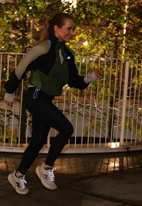 Moteris bėga lauke naktį, vilkėdama žalią ir juodą striukę, juodas kelnes ir šviesiai rudas sportinius batelius su atspindinčiomis raišteliais.