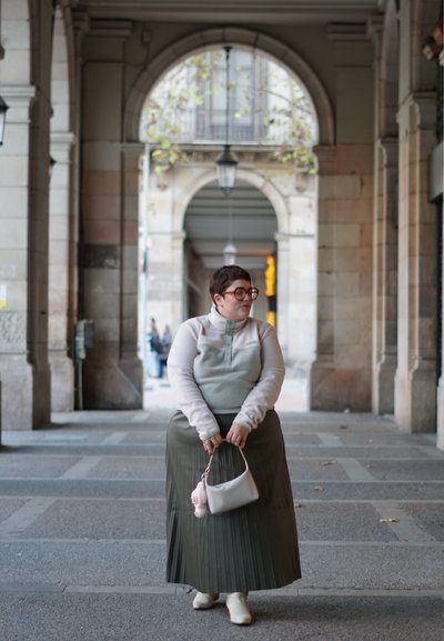 Top de forro polar gris claro y verde menta con cremallera de cuarto, combinado con una falda de oliva con pliegues. Los accesorios incluyen un pequeño bolso blanco y botas de tobillo.