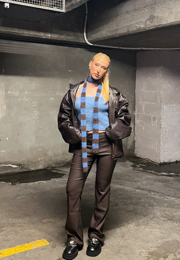 Barna bőr, túlnyújtott dzseki, kék bolyhos crop top, csíkos sál, barna csíkozott nadrág és vaskos fekete cipők fémes díszítéssel.