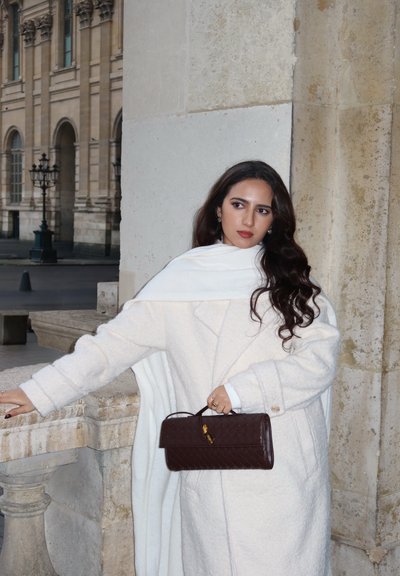 Abrigo blanco de mezcla de lana con acabado texturizado y silueta sobredimensionada, combinado con un bolso tejido color marrón oscuro con detalles metálicos dorados.