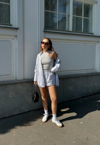 Lyseblå og hvite stripete oversized skjorte, grå utenermetopp, matchende shorts, hvite joggesko, svart veske og solbriller.