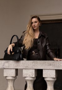 Smeđa kožna jakna s krojem koji prati tijelo, uparena s odgovarajućim remenom i crnom torbom s zlatnim detaljima. Glatka tekstura, minimalistički dizajn.