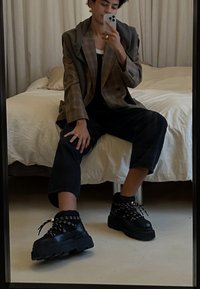 Χοντρές μαύρες πλατφόρμες αθλητικά παπούτσια με παχιές σόλες, υφές και πλεξούδες κορδόνια, συνδυασμένες με μπαλκονέ μαύρο παντελόνι και μια μεγάλη καρό σαλοπέτα.