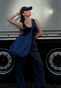 Large navy blue textured shoulder bag with ruffled surface, featuring a wide strap and ample space. Accessorized with silver jewelry.