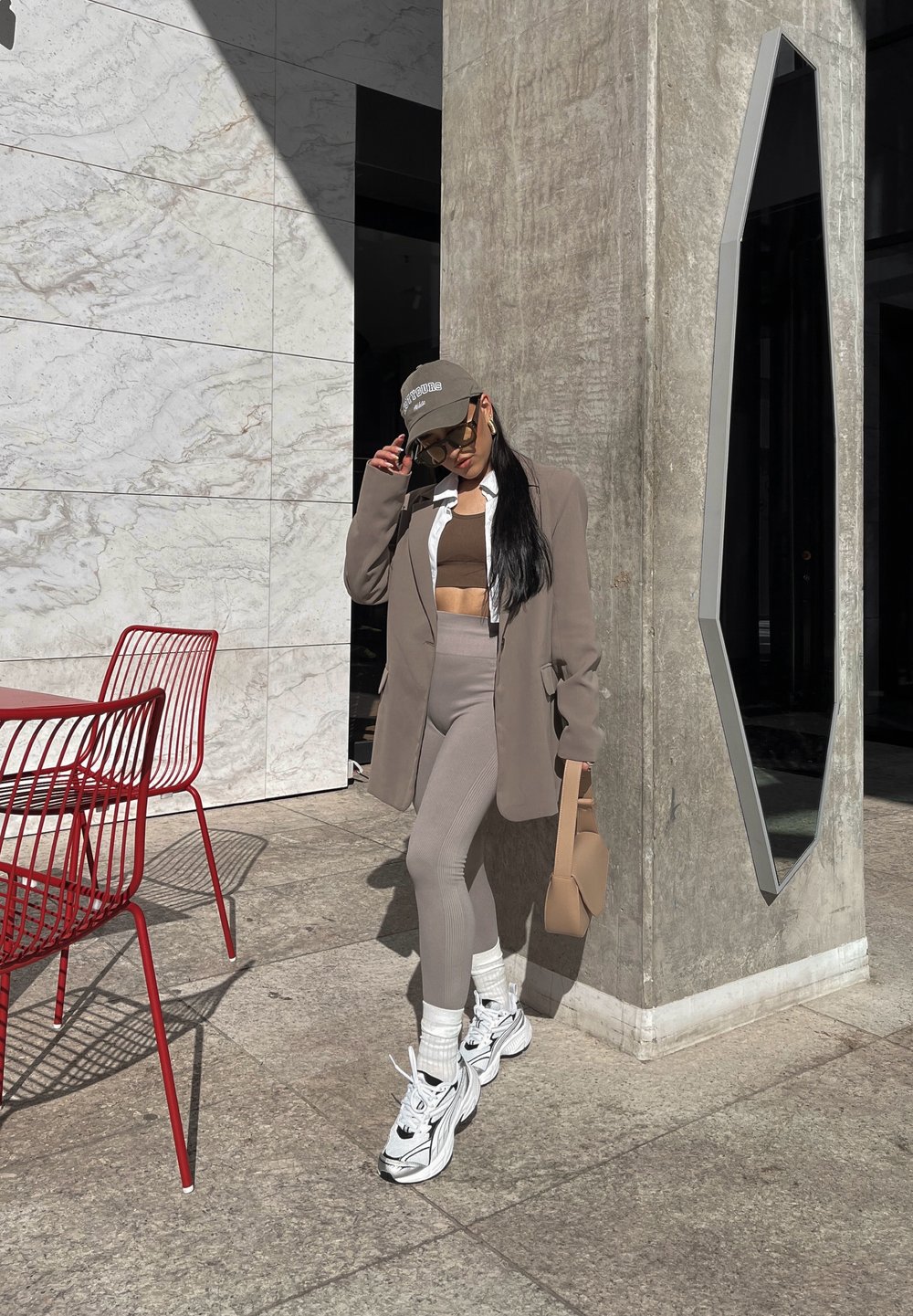 Μόδα με ένα ανοιχτό καφέ σακάκι, κοντό καφέ τοπ, αντίστοιχες κολάν, λευκά αθλητικά παπούτσια και γκρι καπέλο. Μινιμαλιστικά αξεσουάρ.