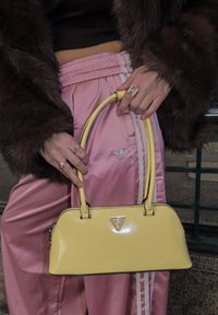 Keltainen patenttinahkainen käsilaukku, jossa on kaareva muotoilu, lyhyet kahvat ja hopeanväriset metalliosat. Etupuolella on kolmiomainen brändilogo.