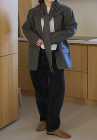 Veste grise oversize, T-shirt blanc, écharpe grise, jean sombre et chaussures marron. Tissu texturé et coupe décontractée.