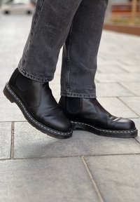 Stivaletti neri in pelle con pannelli laterali elastici, dotati di una suola nera texturizzata e cuciture bianche a contrasto lungo il bordo.