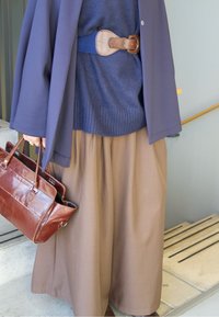 Pantaloni maro cu falduri și picioare largi, pulover tricotat bleumarin, palton bleumarin, geantă de mână din piele maro și o curea lată maro cu detalii cu cataramă.